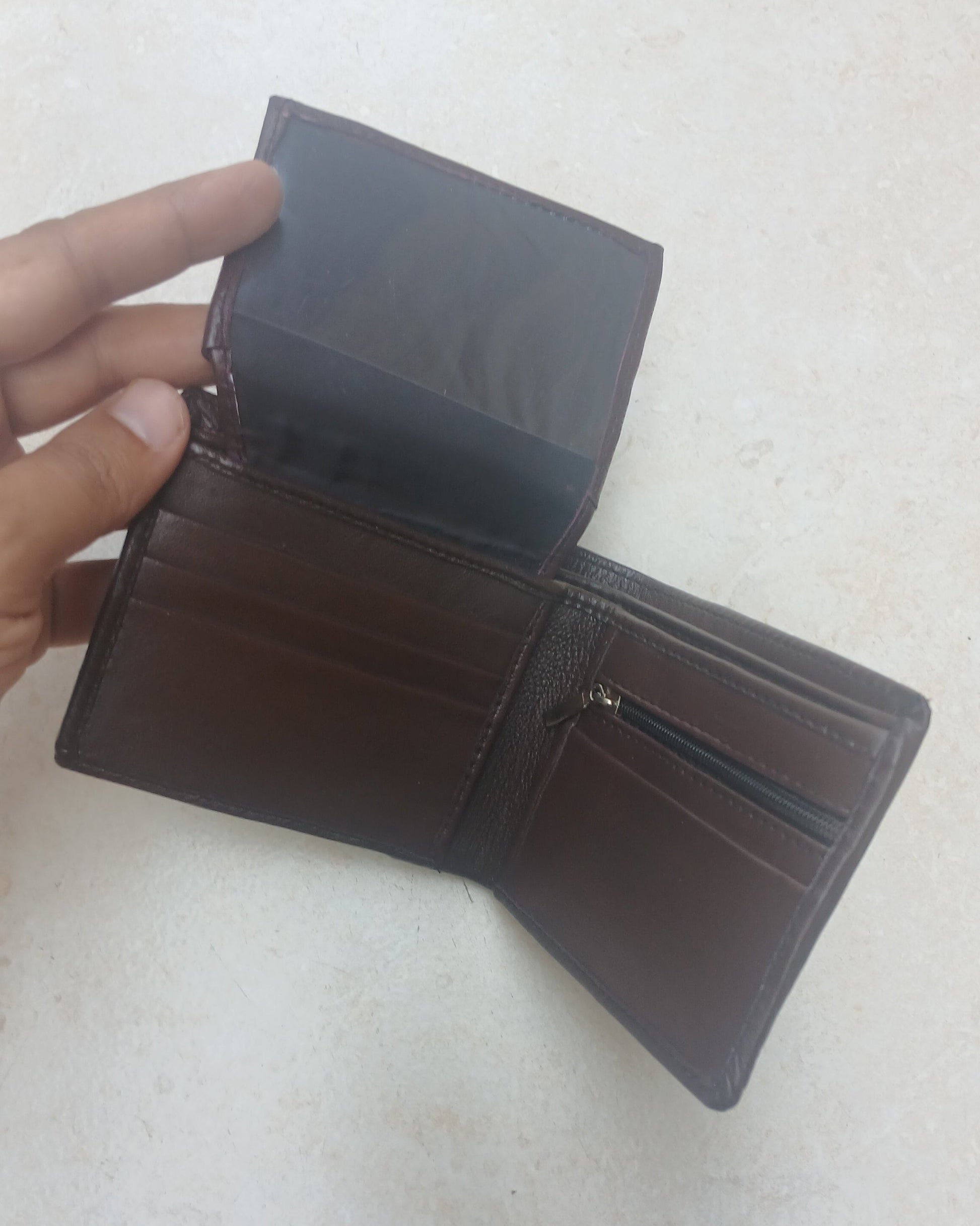 Brown leather wallet held open by a hand on a light gray background